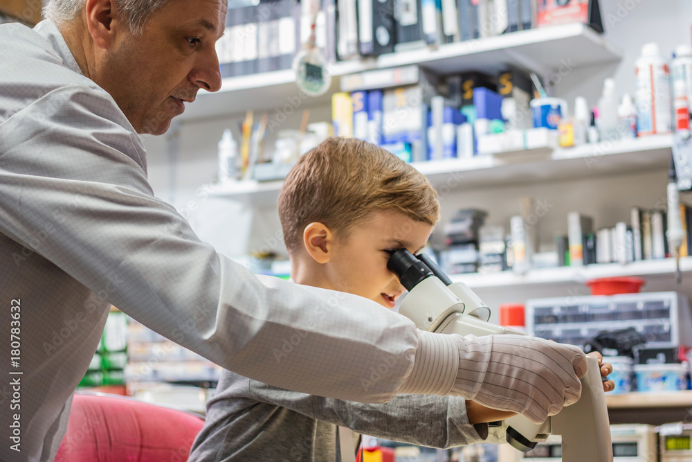 Teacher and little boy examining something through the microscope in laboratory.