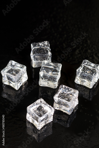 Ice cubes with drops of water on the black background with reflections
