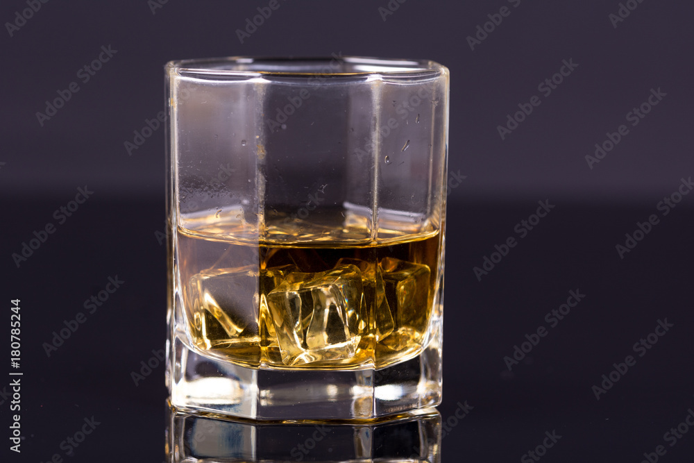 Octagon square glass with whiskey and ice cubes on the black background with reflections