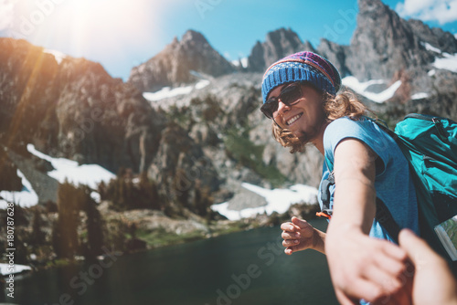 Young hiking couple with backpacks traveling, woman guiding and guy following by the hand into mountain wilderness
