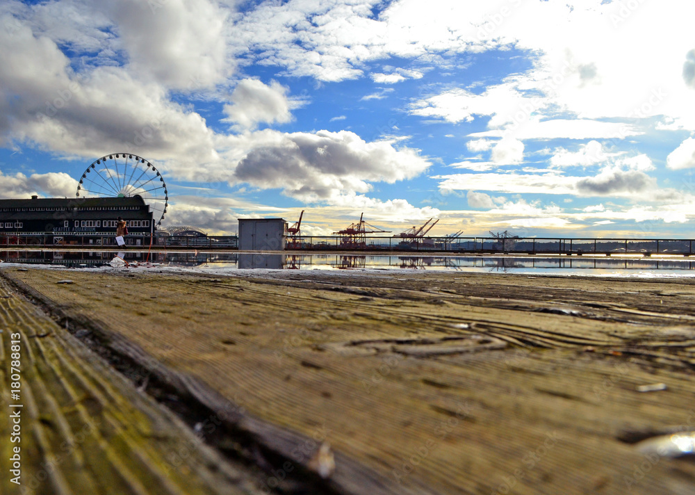 Landscape view of the waterfront in Seattle, Washington, USA from a wooden pier after rain with a wide pudle in which the clouds are reflected.  