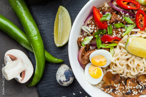 Noodles with beef meat, chili peppers and mushrooms in bowl on dark stone background. Asian Cuisine Pasta. Top view. 