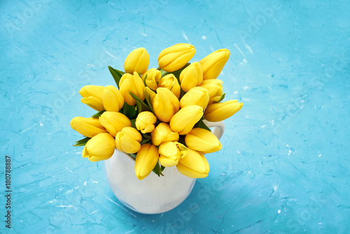 Yellow tulips in vase on blue background. Bouquet. Copy space, top view.