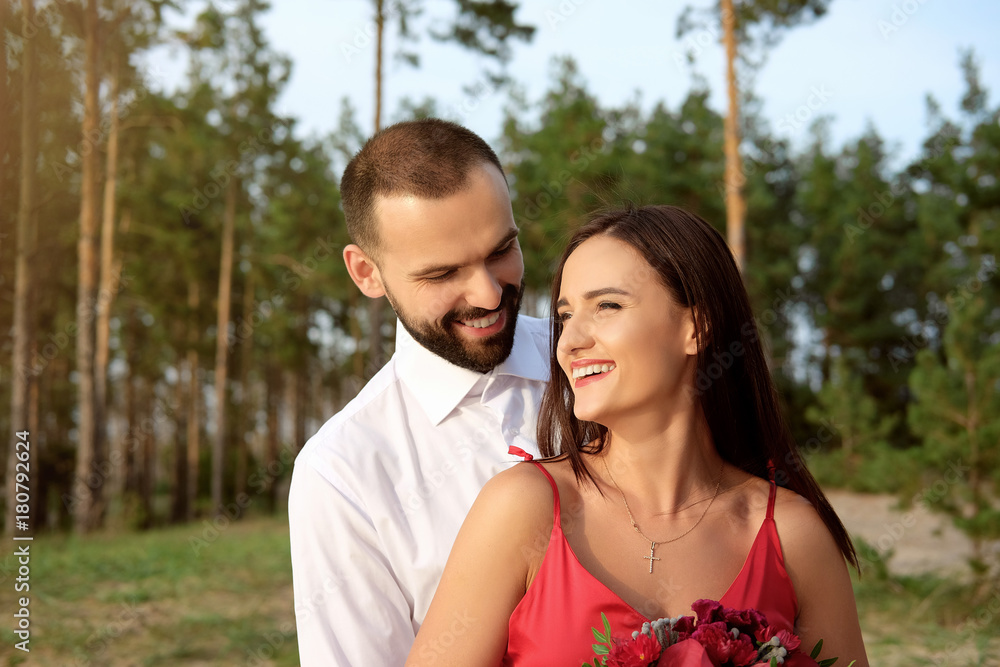 Happy smiling couple of lovers hugging and holding red bouquet of flowers.