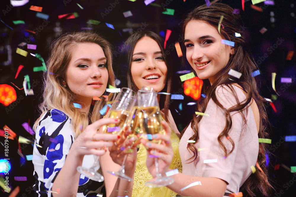 three pretty young girls with glasses of champagne having fun at a party in a nightclub.