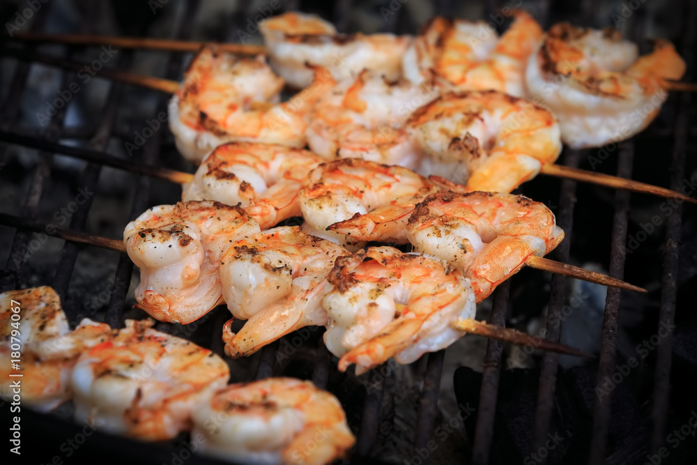 Large shrimps on skewers are roasting on grill