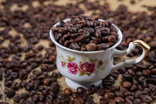 Coffee cup with purple flowers filled with beans surounded with beans on sackclothe