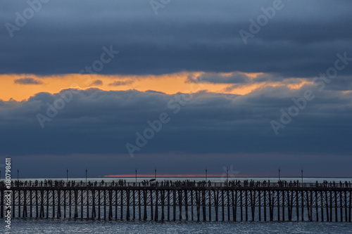 People on an ocean pier silhouetted against dramatic evening sky with clouds