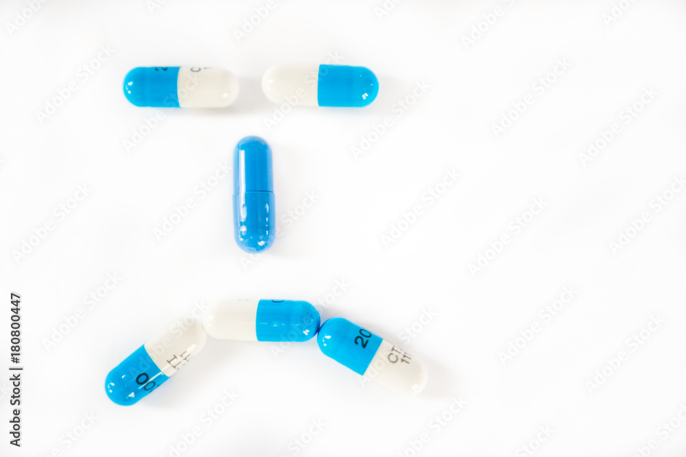 White and blue pills or capsules on white background forming a sad, frown, angry face White and blue pills or capsules on white background forming a sad, frown, angry face