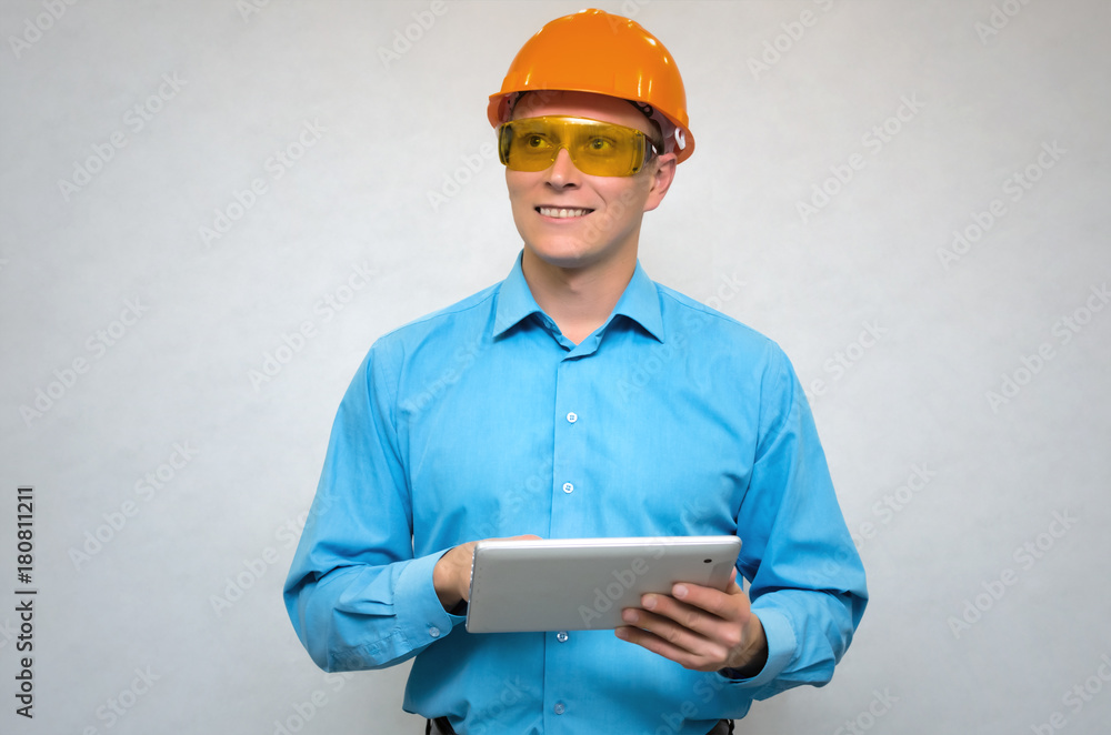 Happy builder worker in a hardhat using a tablet computer in his hands, smiles and looks up isolated. Engineer learning construction plans. Happy builder worker in a hardhat using a tablet computer in his hands, smiles and looks up isolated. Engineer learning construction plans.
