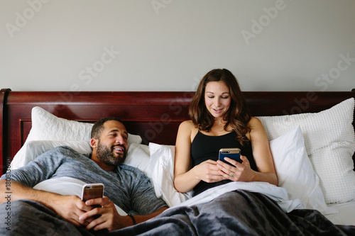 Black and white couple texting in bed