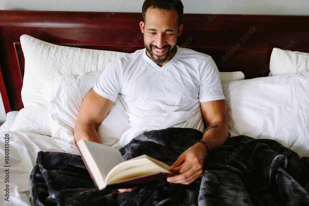 Black man reading a book in bed for fun Black man reading a book in bed for fun
