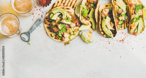 Healthy corn tortillas with grilled chicken, avocado, fresh salsa, limes and beer in glasses over light grey marble table background, top view, copy space. Gluten-free, allergy-friendly food concept