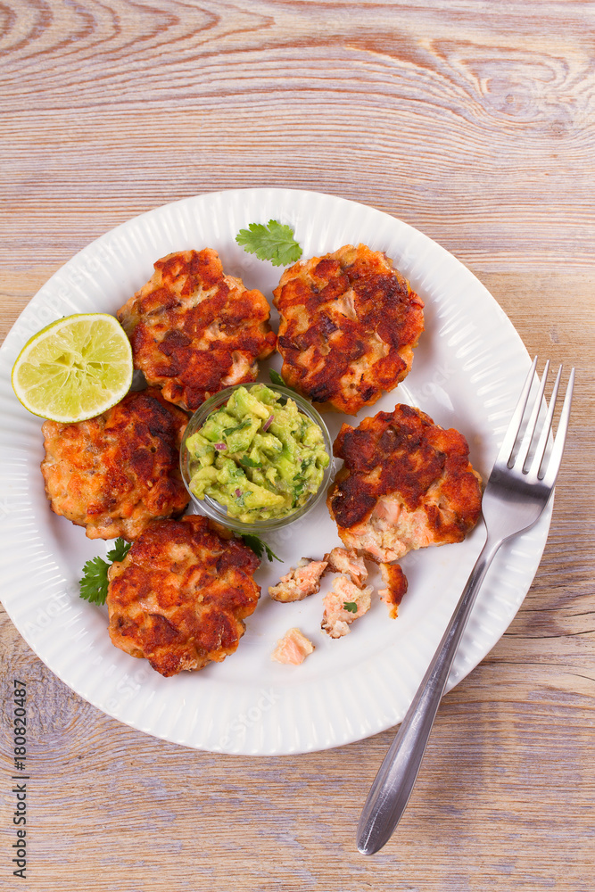 Salmon patties or cakes, lime and avocado on white plate. Fritters of fish. Salmon burgers. Healthy snack or take-away lunch bites, overhead