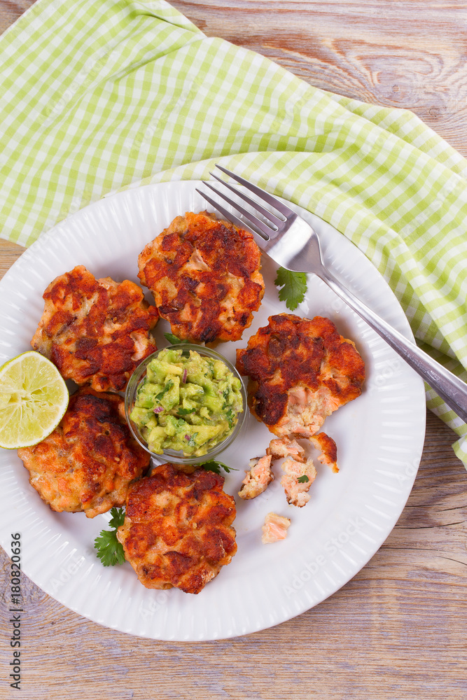 Salmon patties or cakes, lime and avocado on white plate. Fritters of fish. Salmon burgers. Healthy snack or take-away lunch bites, overhead Salmon patties or cakes, lime and avocado on white plate. Fritters of fish. Salmon burgers. Healthy snack or take-away lunch bites, overhead