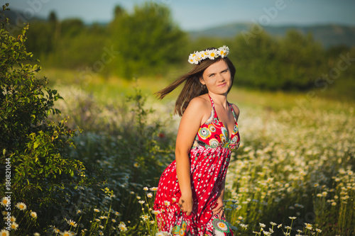 Charming adorable young lady woman dark brunette hairs and green eyes tender sexy posing with flowers wreath on head top and huge bouquet of wild daisy chamomile wearing stylish dress.