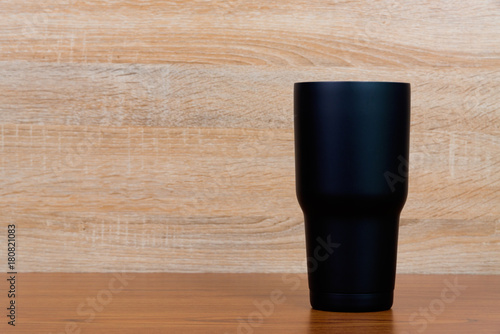 Black colour stainless steel tumbler or cold storage cup on wood background.