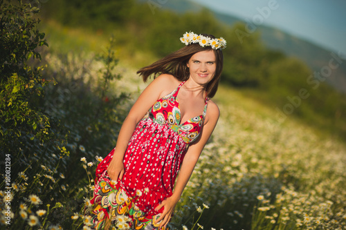 Charming adorable young lady woman dark brunette hairs and green eyes tender sexy posing with flowers wreath on head top and huge bouquet of wild daisy chamomile wearing stylish dress. photo