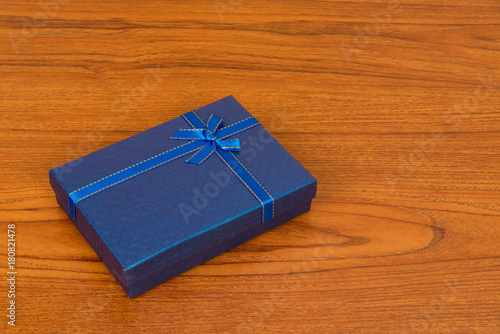 Blue box with ribbon bow on wooden table with copy space for season or greeting and merry concept. © pookpiik