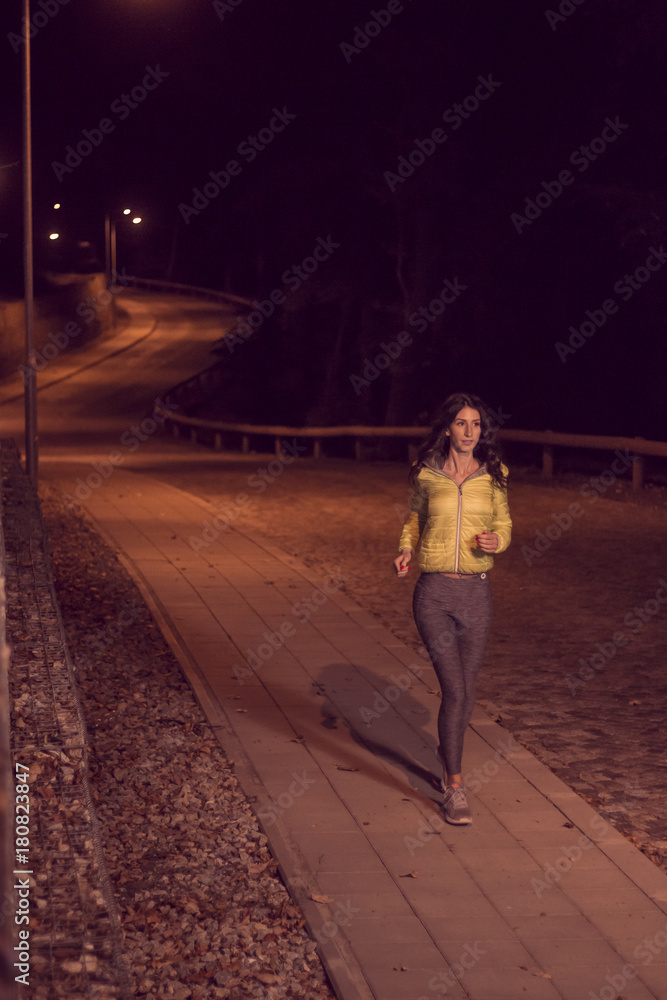 one young woman, alone one person, jogging sidewalk, outdoors night nighttime, street lights, sport clothes, road pavement
