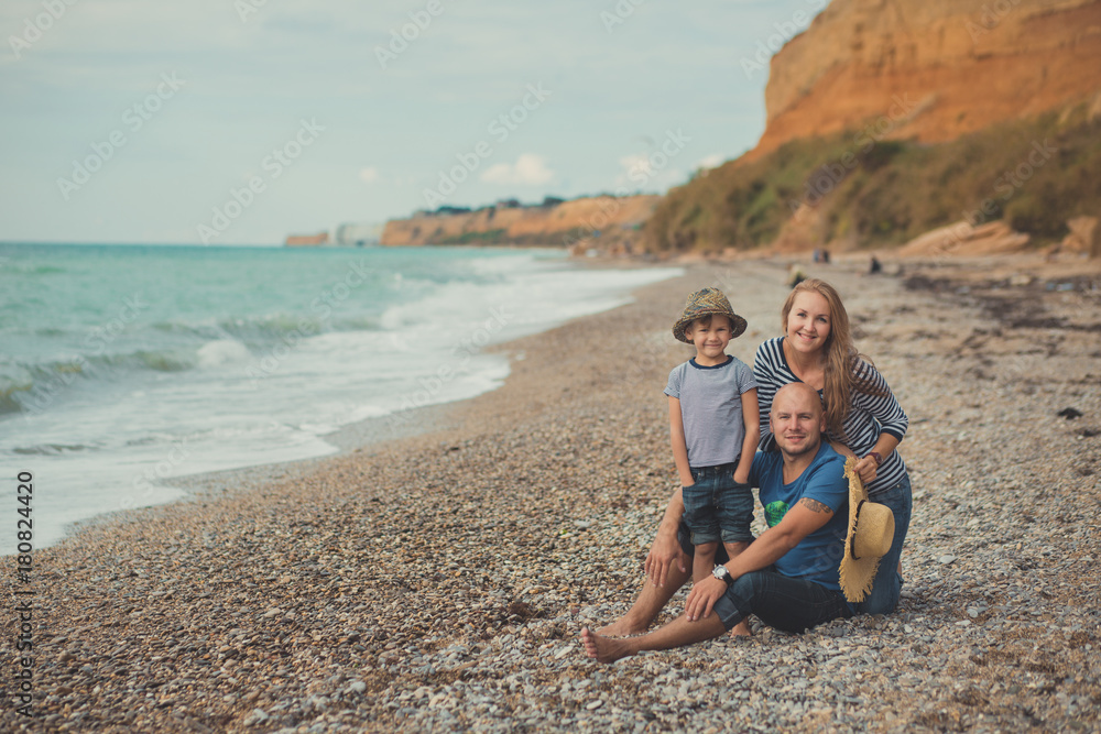 Lovely amazing scene of happy family of handsome father beautiful lady mother and cute little son boy posing together of sea side ocean stone beach on vacation relax wearing stylish clothes