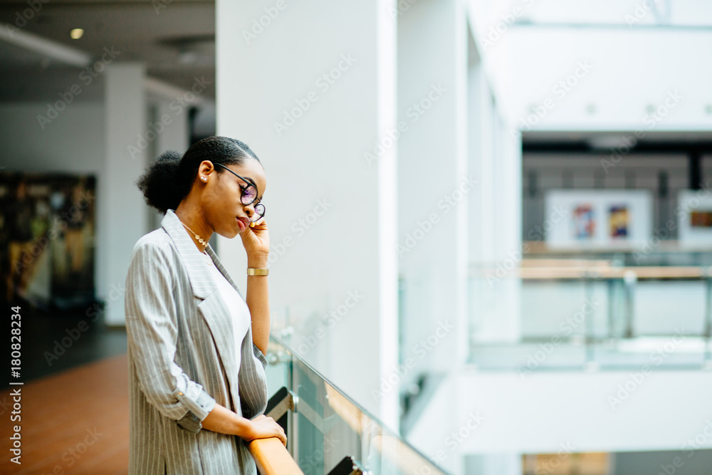 Obraz premium Serious african business student woman standing at railing in business center or shopping mall. Side view. Lifestyle, leisure and people concept.