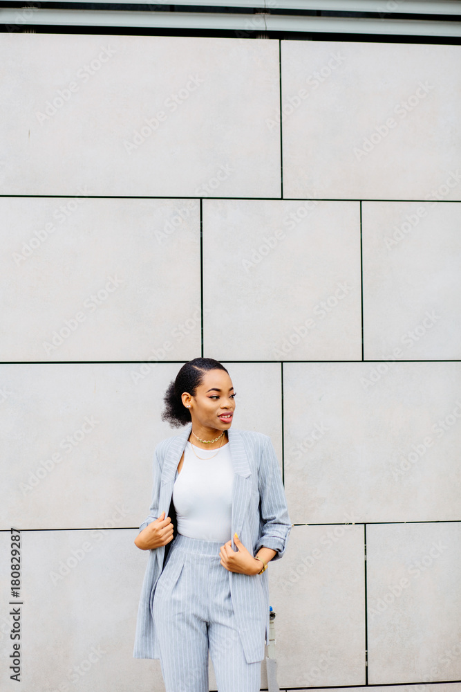 Verical portrait of african business woman in gray suit and red shoes over beige wall background. Lifestyle, leisure and people concept.