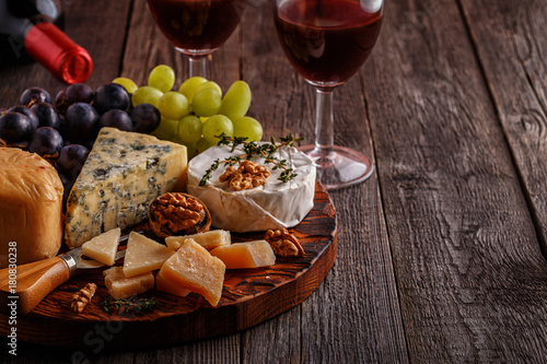 Cheese, nuts, grapes and red wine on wooden background.