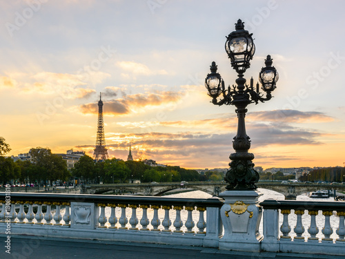 One of the Art Nouveau style street lights of the Alexander III bridge in Paris with the Eiffel Tower in the background at sunset.