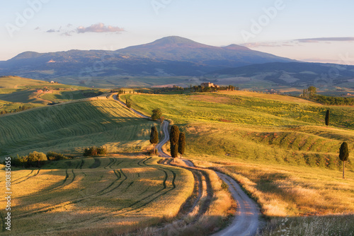 Magnificent spring landscape at sunset.Beautiful view of typical tuscan farm house, green wave hills, cypresses trees, magical sunlight, beautiful golden fields and meadows.Tuscany, Italy, Europe