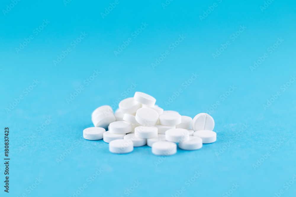 Close up white pills on blue background with copy space. Focus on foreground, soft bokeh. Pharmacy drugstore concept