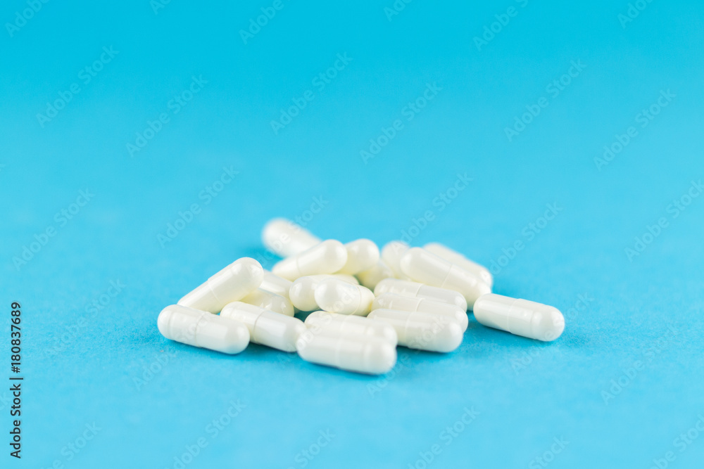 Close up white capsules on blue background with copy space. Focus on foreground, soft bokeh. Pharmacy drugstore concept