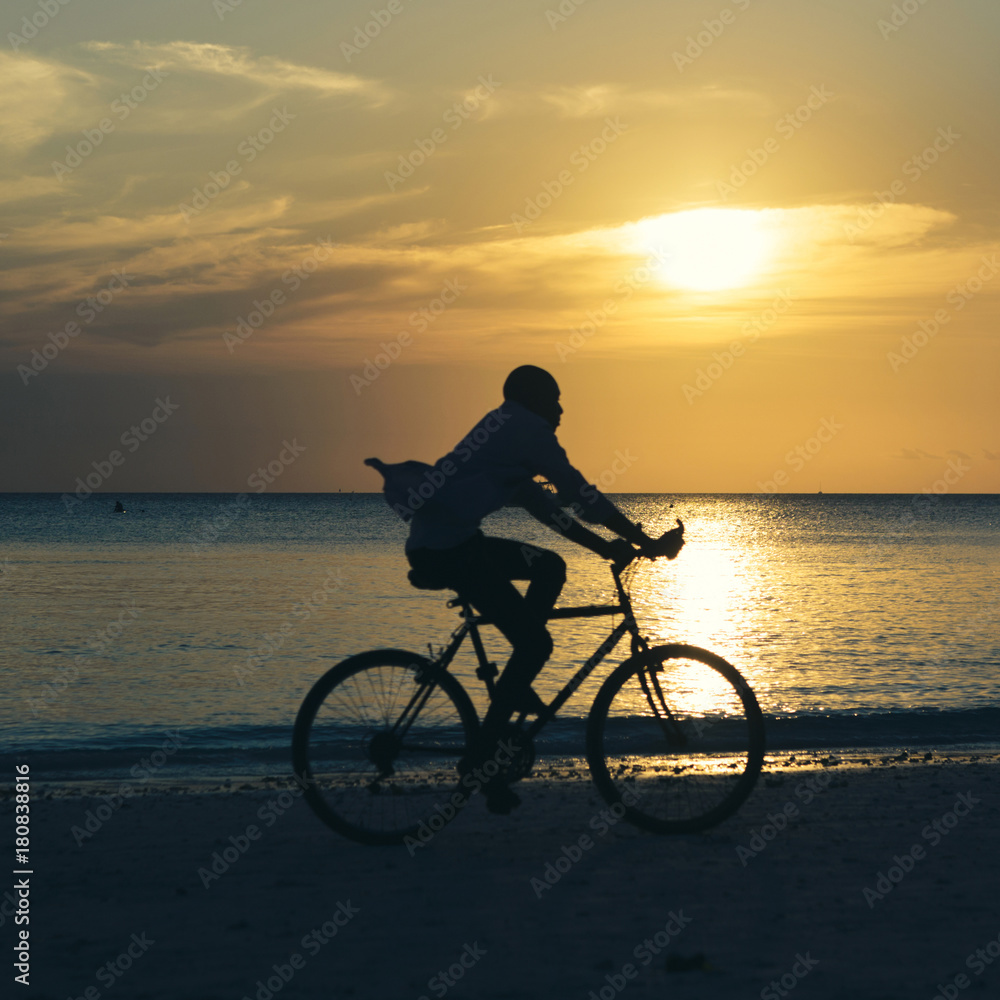 Fototapeta premium Man riding bicycle at sunset along the ocean coast