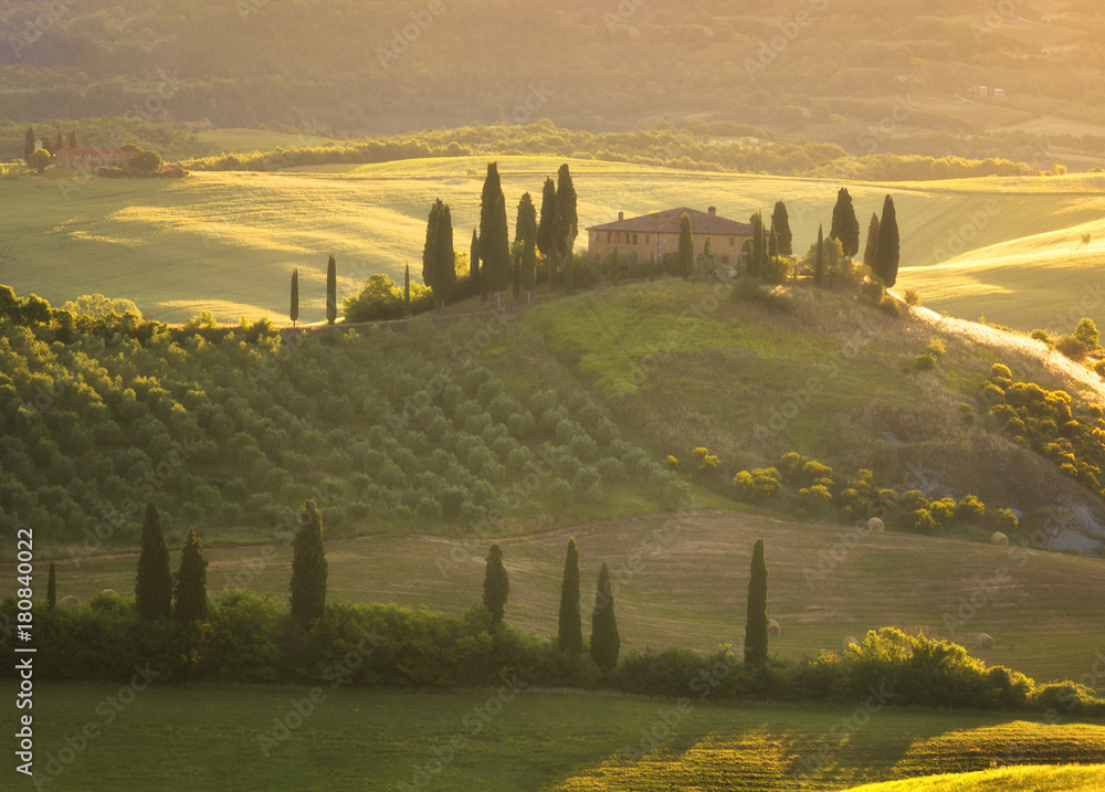 Magnificent spring landscape at sunrise.Beautiful view of typical tuscan farm house, green wave hills, cypresses trees, hay bales, olive trees, beautiful golden fields and meadows.Italy, Europe