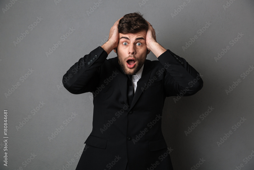 Close-up portrait of shocked young businessman holding his head, looking at camera Close-up portrait of shocked young businessman holding his head, looking at camera