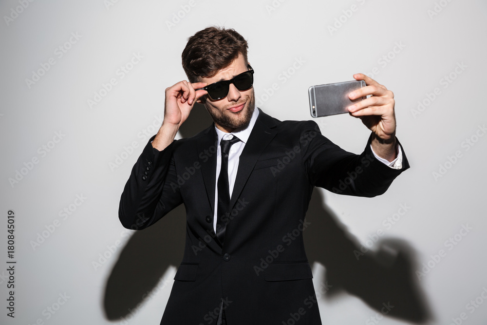 Playful macho in black classic suit and sunglasses taking selfie on smartphone Playful macho in black classic suit and sunglasses taking selfie on smartphone