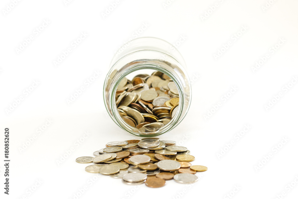 Close up coins in glass jar on white table. Coins scattered around. Isolated on white background. Close up coins in glass jar on white table. Coins scattered around. Isolated on white background.