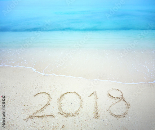 Happy New Year 2018  lettering on the beach with wave and clear blue sea. Numbers 2018 year on the sea shore  message written in the white sand on the tropical beach background. Concept for holiday.