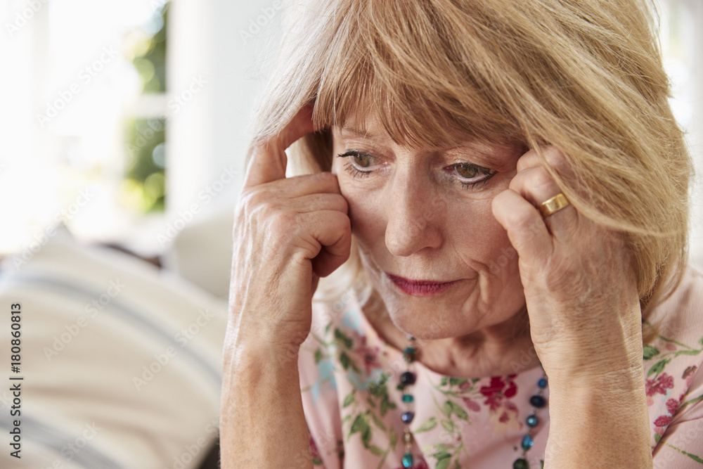 Senior Woman Sitting On Sofa At Home Suffering From Depression