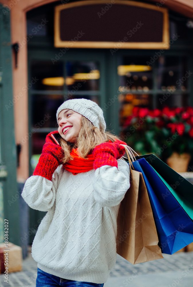 Obraz premium Beautiful smiling woman with shopping bags near shop with gift calling smart phone.