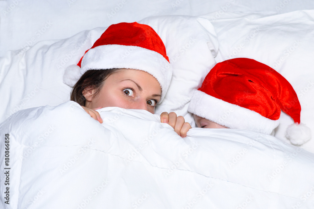 The terrified mother lying in bed with her baby and hides under a white blanket. The baby is sleeping. A mother with a little baby boy in Santa hats.Afraid of the new year.
The terrified mother lying in bed with her baby and hides under a white blanket. The baby is sleeping. A mother with a little baby boy in Santa hats.Afraid of the new year.