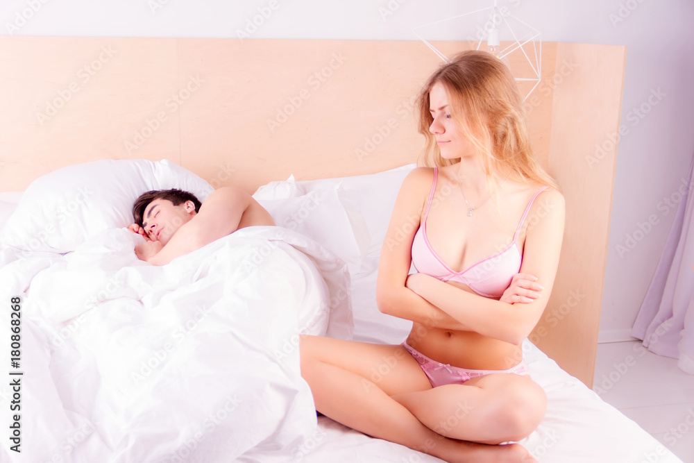 Foto de Sexy, unhappy, angry woman in pink underwear with sleeping happy  man in bed in morning. do Stock