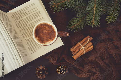 Cup of hot chocolate, book and glasses on brown knitted background. Top view