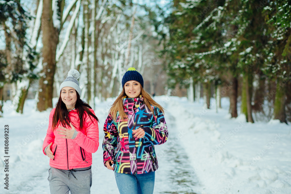 Two young attractive women running in the winter park
