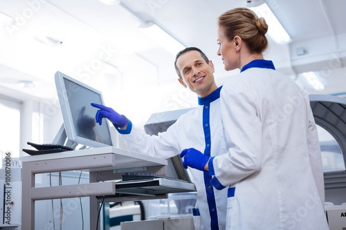 Strong team. Couple of researchers discussing interesting medical case while he pointing at the screen and smiling to her photo