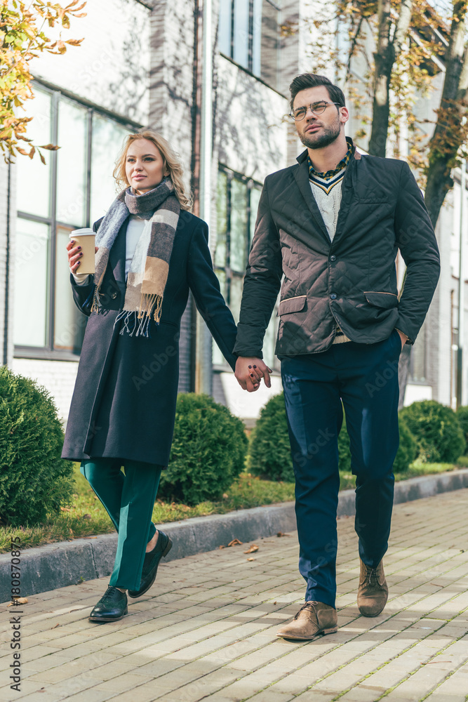 couple with coffee to go walking on street