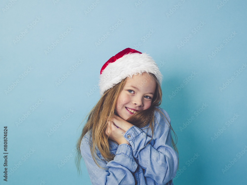 young beautiful blond girl with christmas hat in front of blue backgroubd young beautiful blond girl with christmas hat in front of blue backgroubd