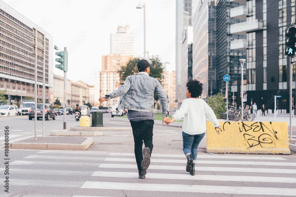 Obraz premium Back view of young multiethnic couple running outdoor in the city holding hands, having fun - happiness, friendship, lovers concept
