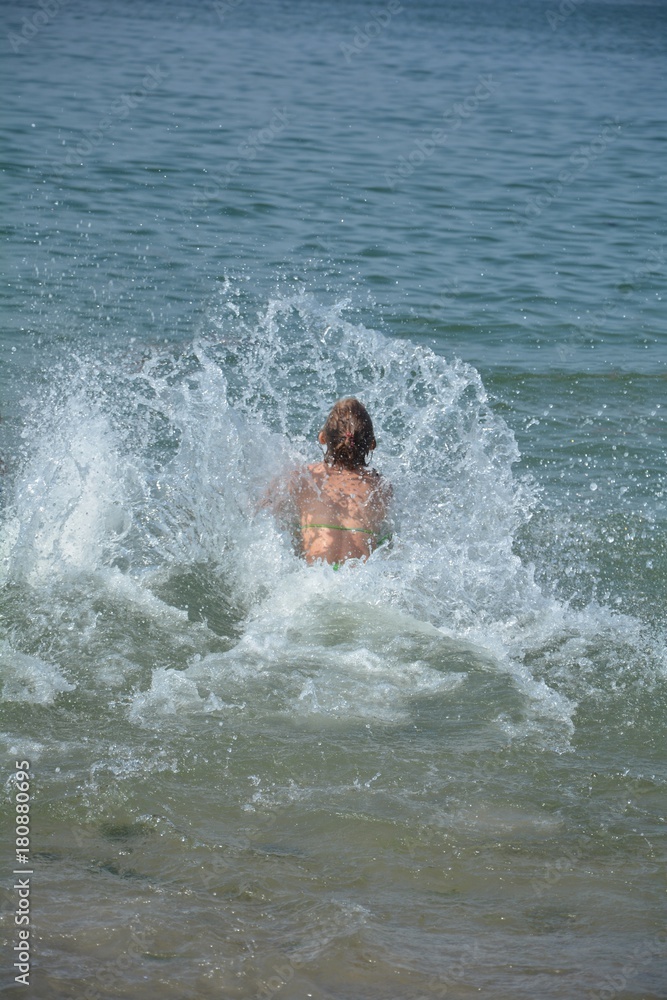 Mädchen im Bikini springt  ins Meer, Wasser spritzt in die Höhe
