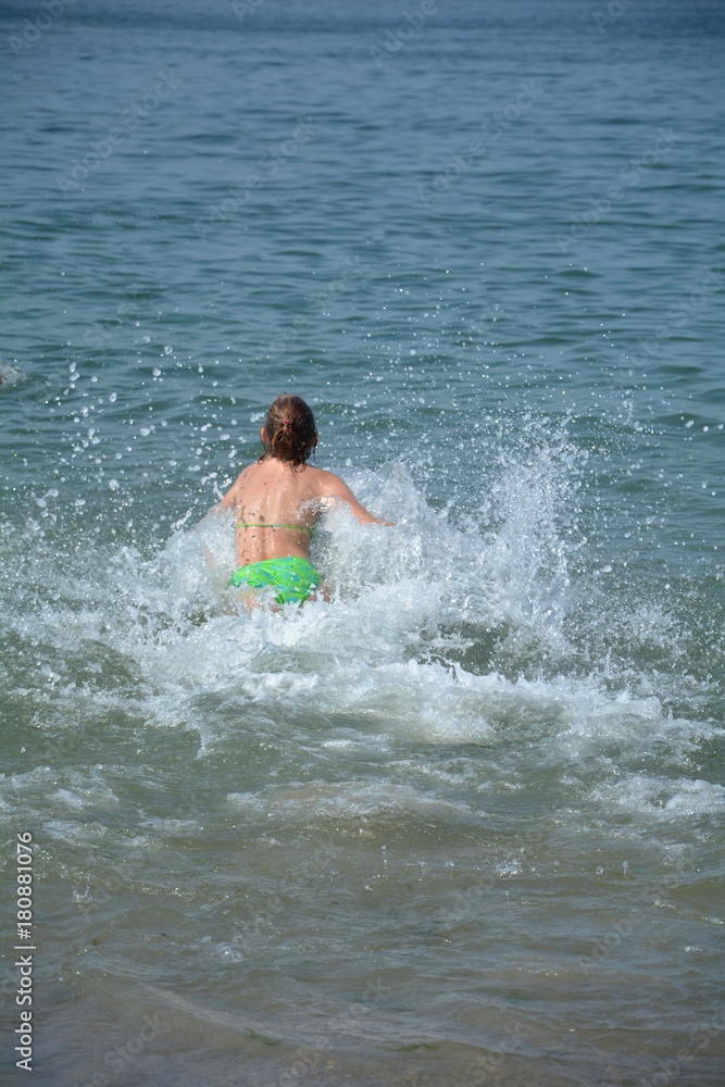 Mädchen von hinten, springt ins Meer,  Wasser spritzt in die Luft